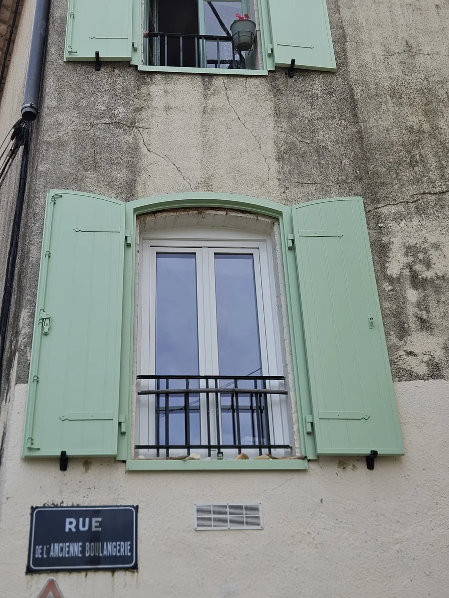 Fenêtre PVC blanche installée sous un cintre extérieur avec volets battants verts à Dions.